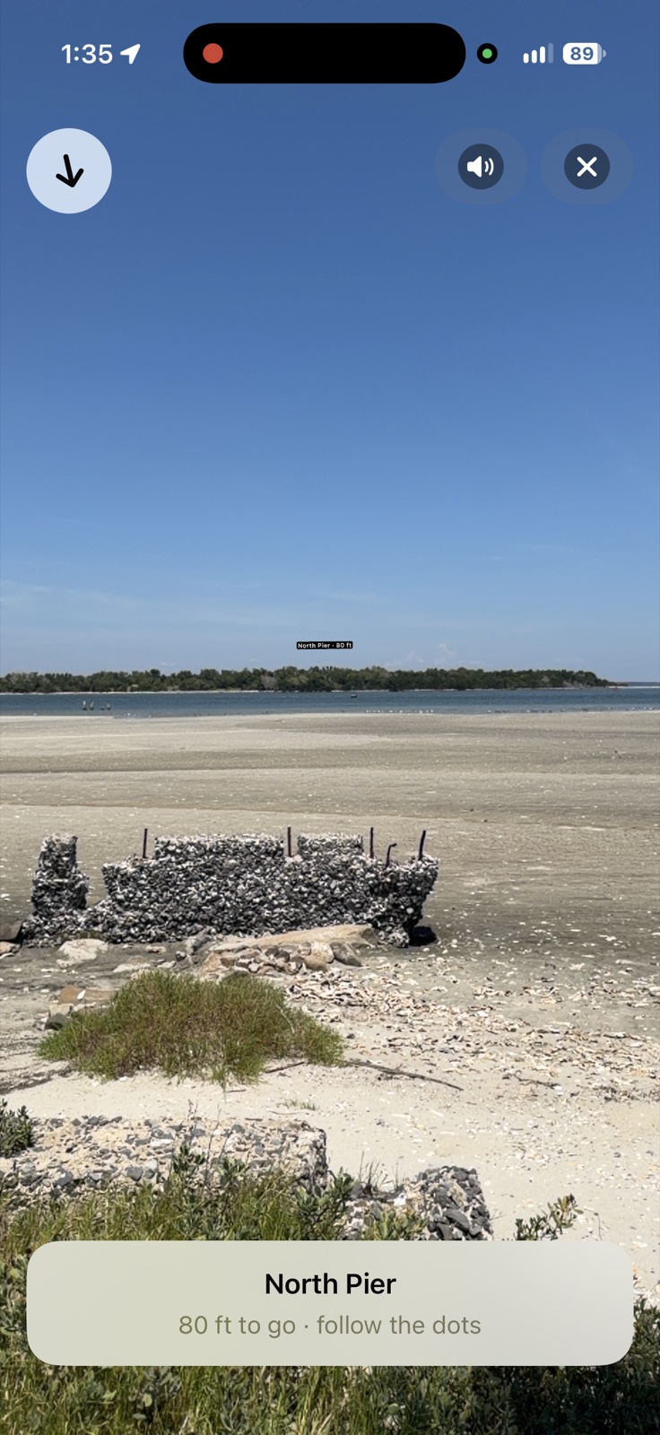 iPhone screenshot of Lookabout's AR walking guide arriving at Fort Pulaski's North Pier: a wide low-tide beach with oyster-shell pier ruins in the sand, a small floating North Pier label in the distance, and a banner reading 80 ft to go, follow the dots.