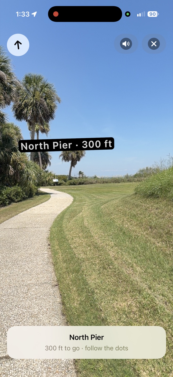 iPhone screenshot of Lookabout's AR walking guide at Fort Pulaski: a floating North Pier · 300 ft label over a shell path curving through palms toward the water, with a banner reading 300 ft to go, follow the dots.